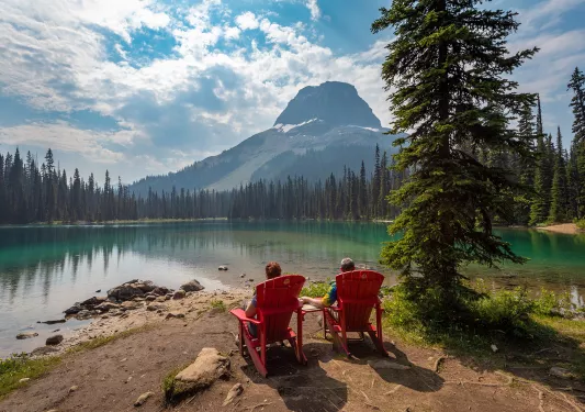 Two guests sitting lakeside, Wapta Mountain in distance.