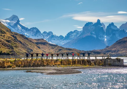 Line of guests on lakeside, arms above head, large mountain vista behind them.