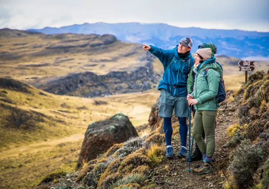 Three guests on hillside trail, one pointing towards something off-frame. 