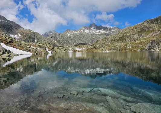 Shot of still lake, craggy rocks dotting lakeside, mountain in distance.