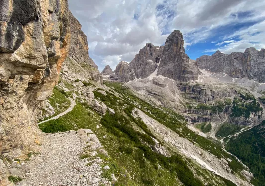 Wide shot of craggy cliffs, trails, valley, mountain in distance.