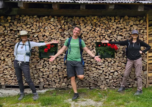 Three guests in front of wooden building, one in center, the other two gesturing to them.