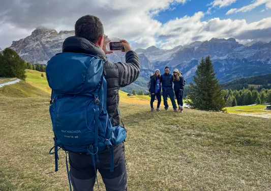 One guest taking photo of other three, mountains behind them.