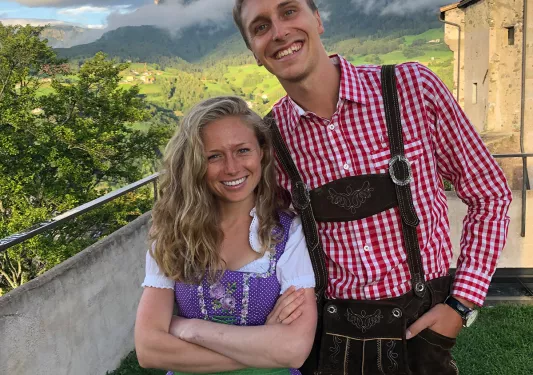 Two locals smiling, large mountains, clouds behind them.