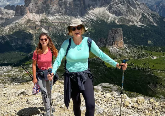 Two guests on hilltop, large, cloud-shaded mountains behind them.