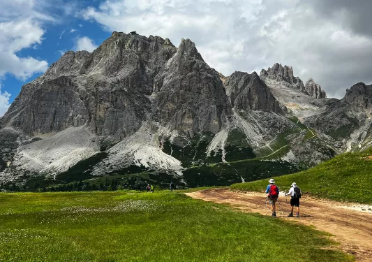 Two guests on trail, hiking towards large mountain in front of them.