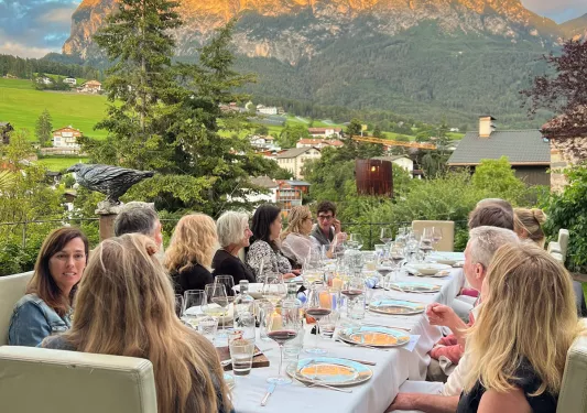 Group of guests at dinner table, sunset-kissed mountains in distance.