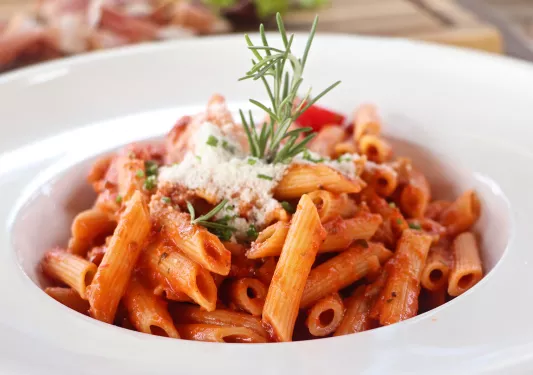 Plate of tomato pasta, cheese, rosemary garnish.