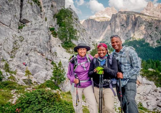 Three guests in hiking gear, craggy cliffside to their right.