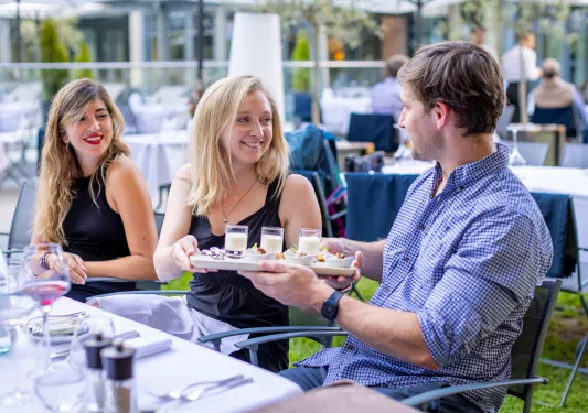 Three guests at dinner, passing tray of dessert to one another.