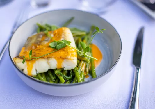 Plate of pan fried fish with an orange sauce, bed of greens.