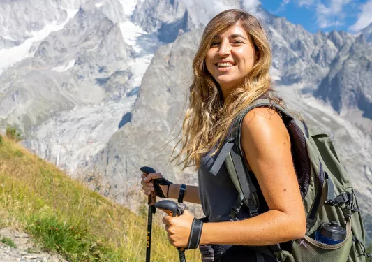 Guest with hiking poles smiling for camera, craggy mountains in distance.