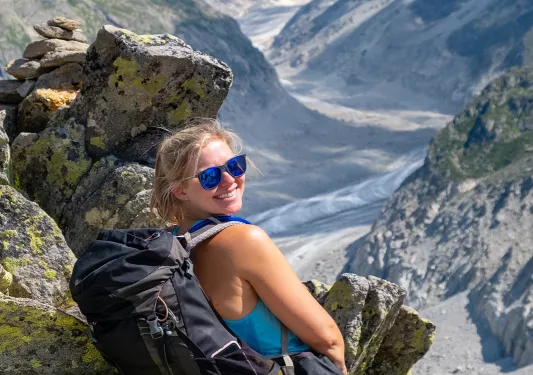 Young guest sitting on rock, smiling at camera, large mountain valley in distance. 