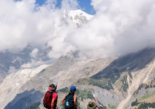 Three guests on hillside, one pointing towards distant mountain.