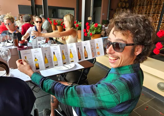 Guest showing large wine list to camera, smiling.
