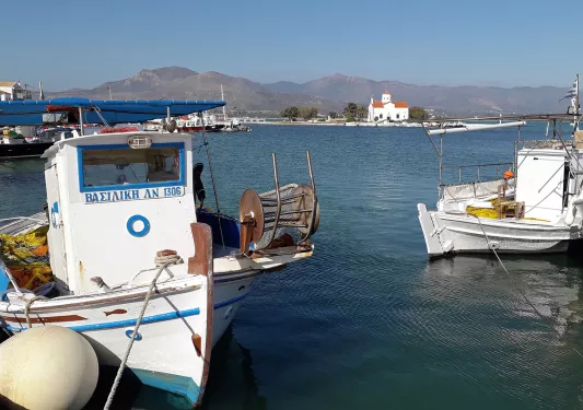 POV shot at boat dock, small fishing boats, small building, mountains in distance.