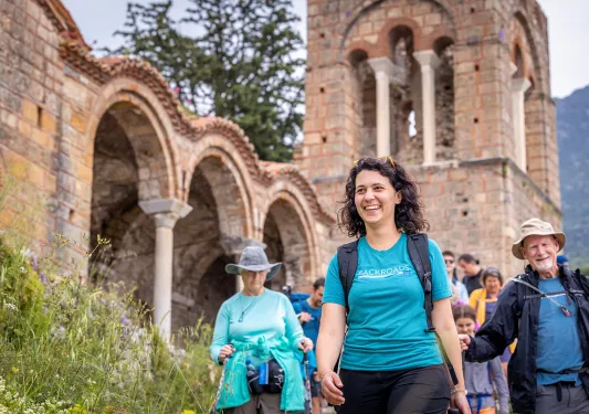 Group of guests walking past stone building, archways, tower behind them.