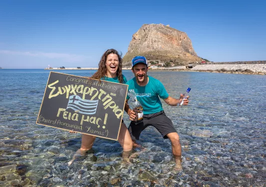 Two leaders holding Greek lettered "Congratulations" signage, standing in shallow water.