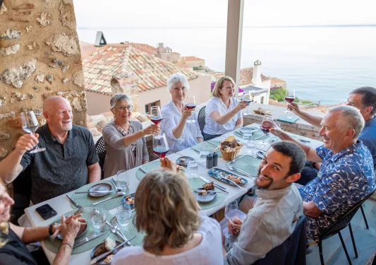 Guests at dinner table, all cheersing wine glasses, overlooking ocean.