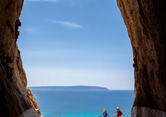 POV shot inside large cave, looking out towards two guests, ocean view.