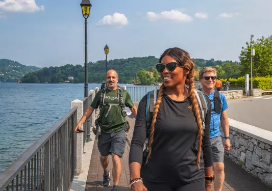 Three guests walking beside lake, road to their right.