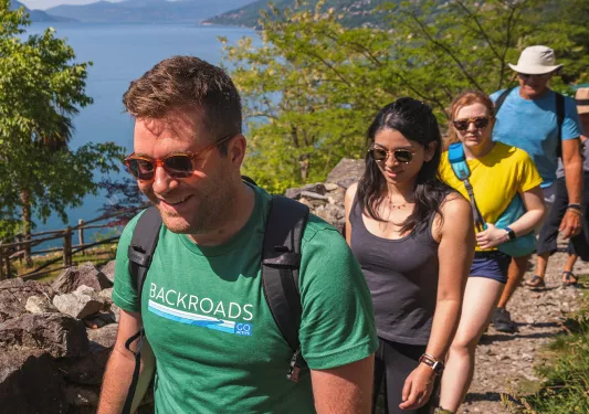 Group of guests walking beside lake, cliffside to their right.