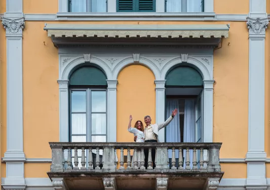 Two guests on balcony, waving to camera. 