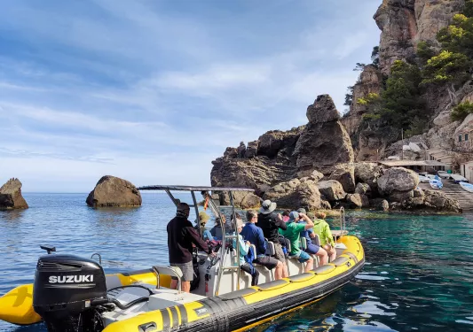 Guests on large dinghy, approaching rocky coastline.