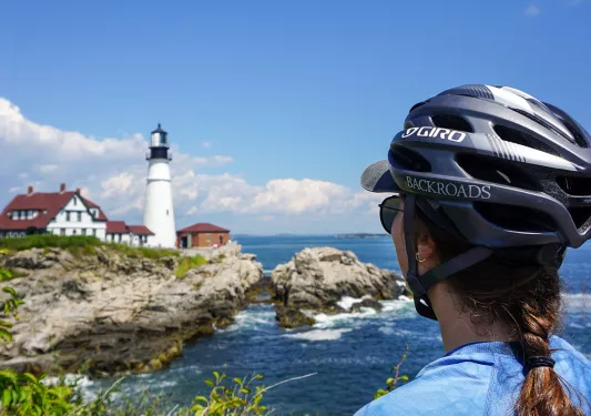 Caucasian woman in a bike helmet looks across a body of water at a lighthouse