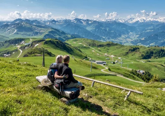 Two hikers sitting on a split log in a grassy field.