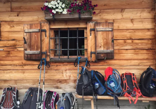 Hiking backpacks piled in front of log cabin.