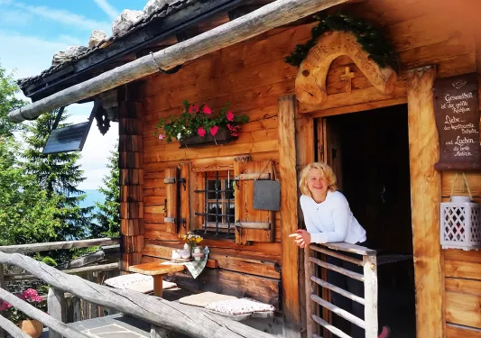 Woman leaning on balcony off of log cabin.