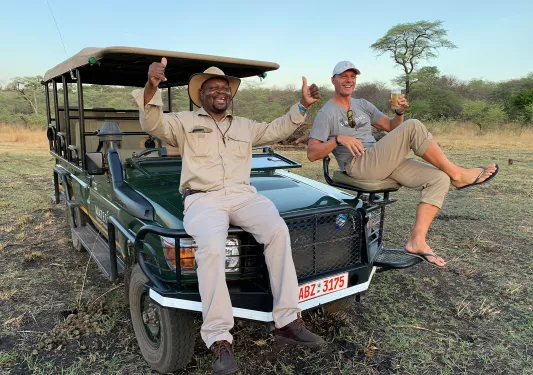 Guide sitting on hood of jeep giving camera thumbs up