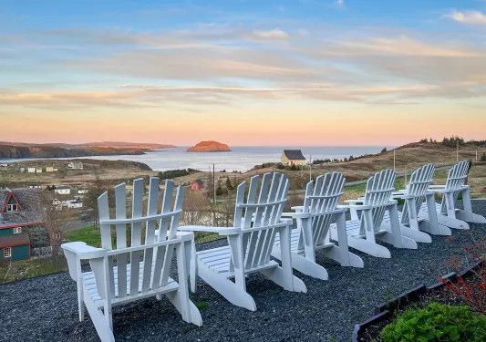 Wide shot of grassy ocean vista, white chairs in foreground.