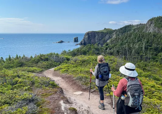 Two guests hiking towards ocean, rocky cliff to their right.
