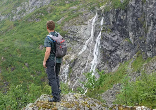 Solo hiker facing away from the camera, looking out at waterfall