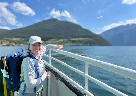 Woman posing for the camera while leaning on boat rail on the water.
