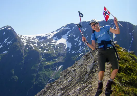 Woman celebrating reaching the summit holding miniature flag of Norway.