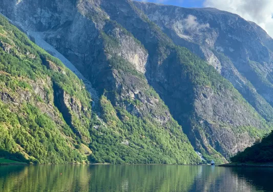 Blue sky and mountainside reflected in a clear Norwegian fjord