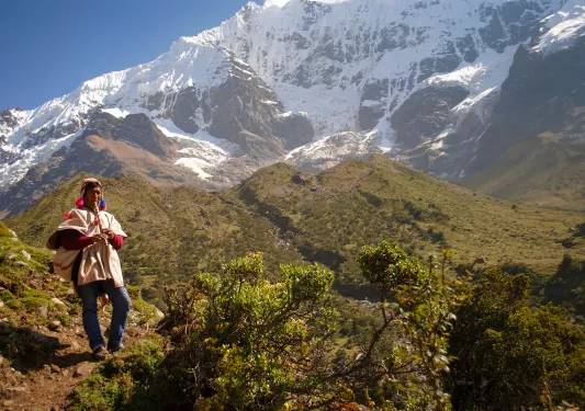Local on hillside playing instrument, snowy mountains, hills behind them.