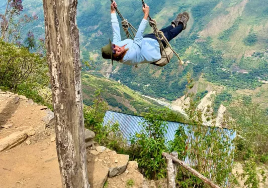 Guest on cliffside swing, overlooking large drop.