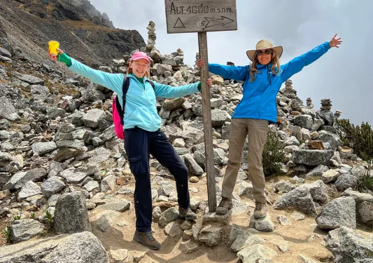 Two guests with "ABRA SALKANTAY" sign, clouds and cliff behind them.