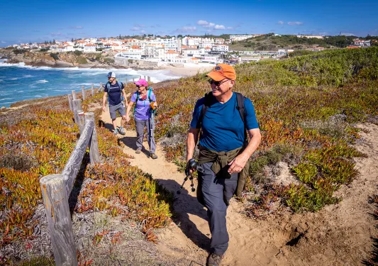 Three guests walking along ocean cliff, beach town behind them.