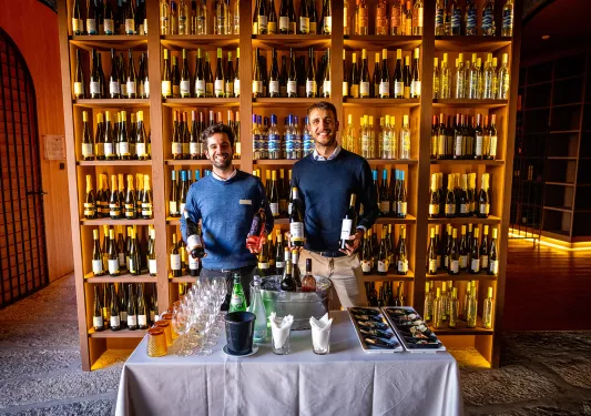 Two local wine sellers, wall of bottles behind them, table in front.