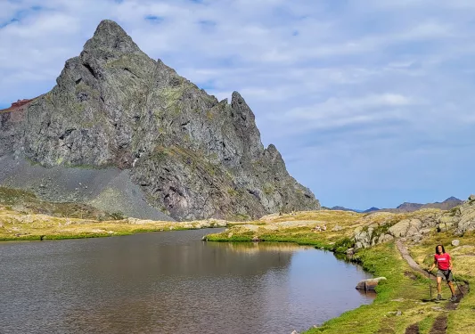 Guest next to small lake, large craggy mountain to her right.