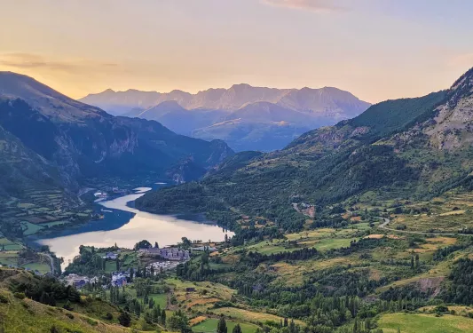 Wide shot of mountain valley town, river running through, sunset.
