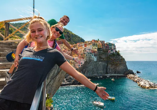 Three guests on cliff, gesturing towards colorful coastal city.