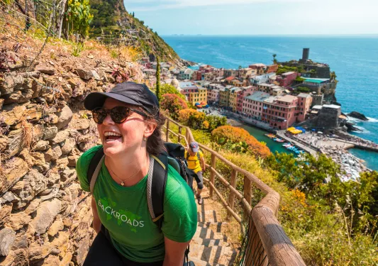 Two guests hiking up rocky trail, colorful coastal town in background.