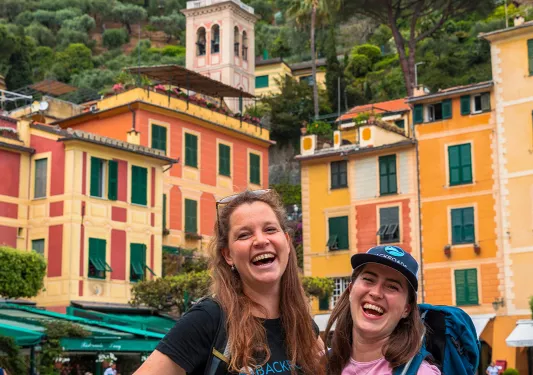 Two smiling guests in front of colorful buildings.