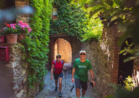 Two guests walking through arched brick walkway, flowers and hanging plants above.